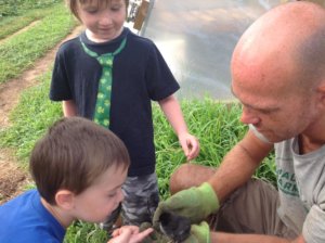 two children looking at baby chick held by man