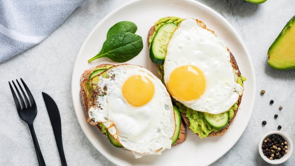 two slices of toast with avocado and sunny side up eggs on top