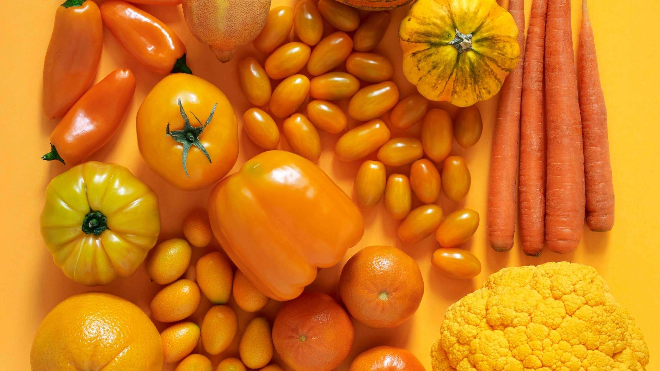 orange fruit and vegetables flatlay on orange background