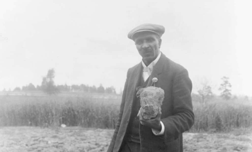 George Washington Carver holding a piece of soil in a field, 1906.