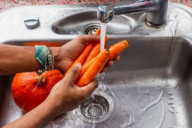 two hands rinsing carrots in sink