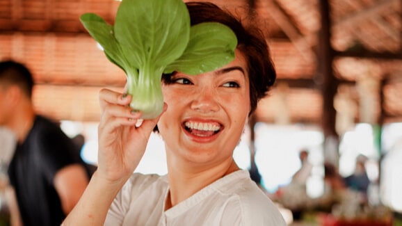 Woman smiling while holding a leafy vegetable